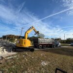 CAT excavator loading a dump trailer with concrete debris during a Florida demolition and hauling job