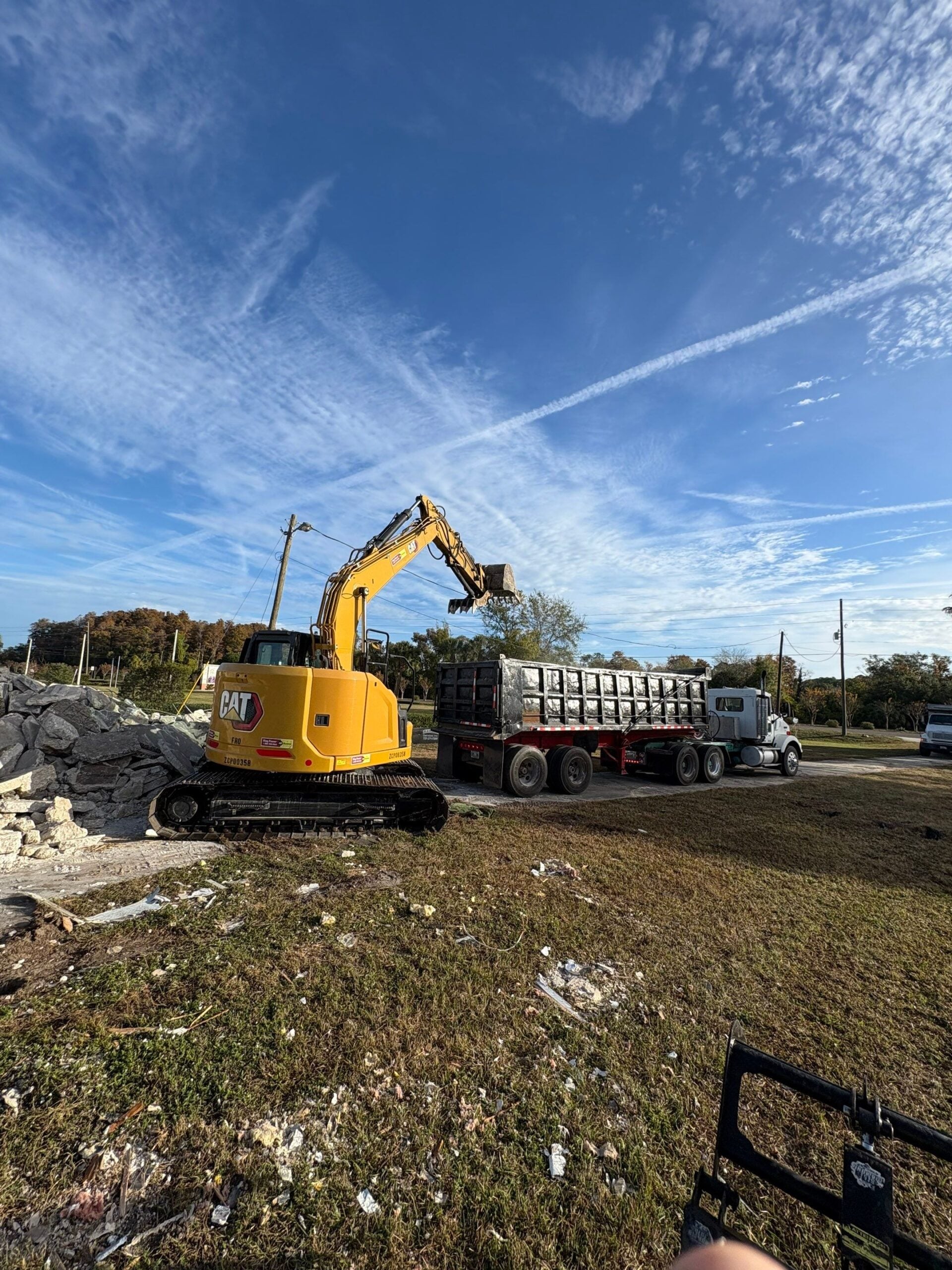 CAT excavator loading a dump trailer with concrete debris during a Florida demolition and hauling job