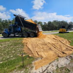 Blue dump truck delivering fill sand for site prep next to a compact excavator in Central Florida