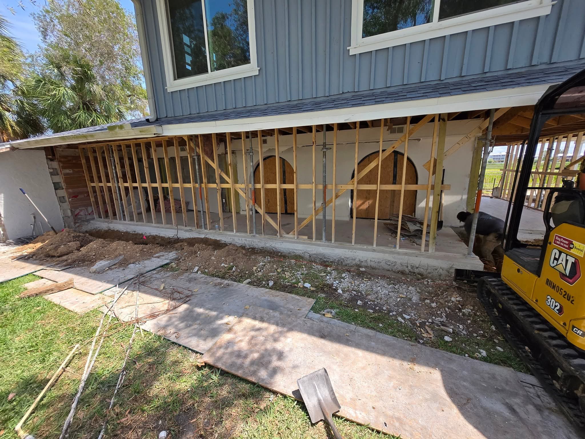 Florida Hauling & Demo CAT mini excavator working on a home addition with the first-floor exterior opened to framing